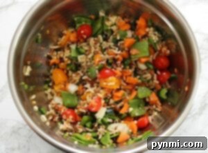 Smoky Stuffed Bell Peppers 4 A metal bowl filled with mixed vegetables, cherry tomatoes, rice, and slices of grilled stuffed peppers sits on a light marble surface.