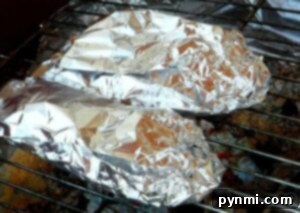 Smoky Stuffed Bell Peppers 5 Two foil-wrapped food items, possibly grilled stuffed peppers, cook on a grill over hot coals.