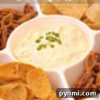 A divided tray showcasing the most incredible beer cheese dip recipe is adorned with chopped green onions and surrounded by a variety of pretzels, tortilla chips, and corn chips.