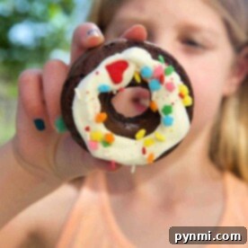 A child proudly holding a chocolate donut made from cake mix, adorned with white icing and colorful sprinkles.