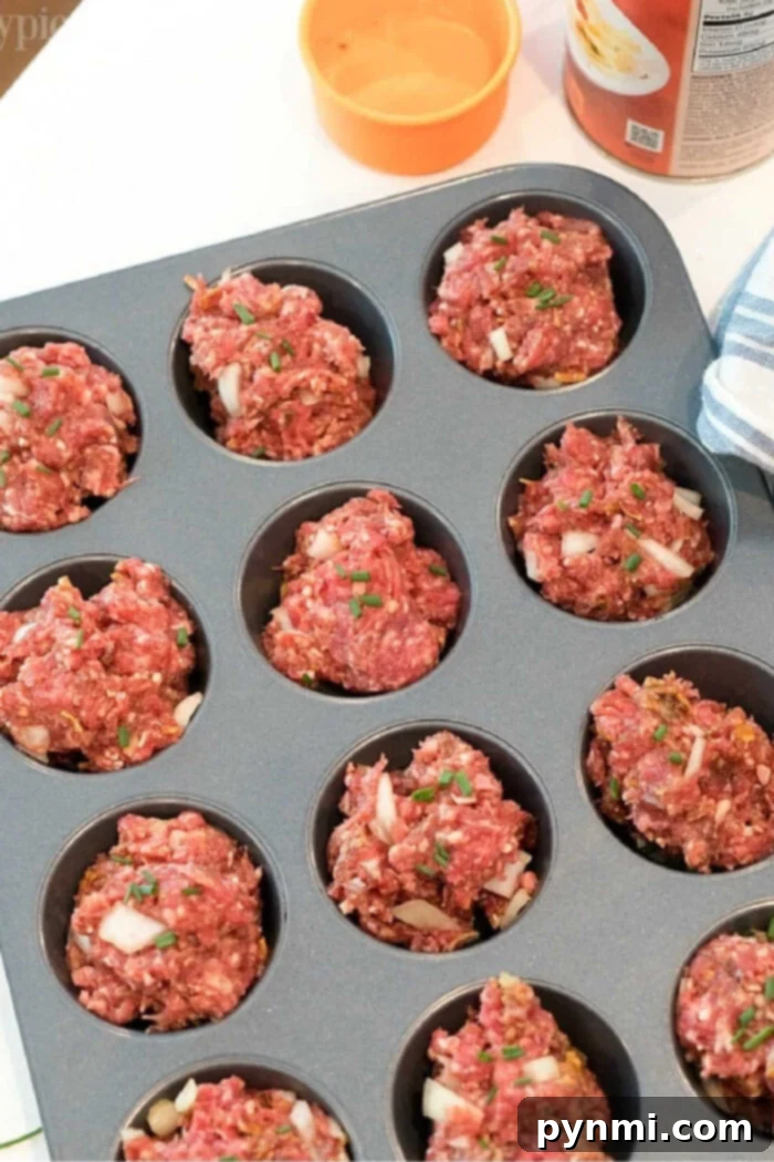 Savory Meatloaf Cups 2 A muffin tin filled with raw meatloaf mixture ready to be baked. The meatloaf muffin recipe portions appear roughly shaped and are topped with bits of onion and herbs. An orange bowl and a tin can are visible in the background.