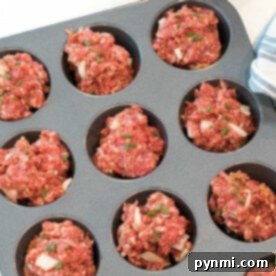 A muffin tin filled with raw meatloaf mixture ready to be baked. The meatloaf muffin recipe portions appear roughly shaped and are topped with bits of onion and herbs. An orange bowl and a tin can are visible in the background.