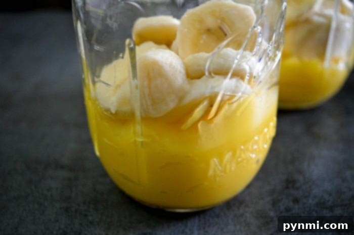 Really easy orange creamsicle drink perfect for Fall. Use fresh fruit and juices to make this frosty creamy Orange Julius drink layered with flavor. Two glasses of orange creamsicle drink, one with an orange slice, on a rustic wooden surface.
