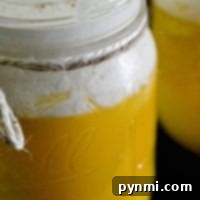A glass jar brimming with creamy yellow pudding evokes the delightful flavor of an orange creamsicle drink, topped with a swirl of whipped cream and a delicate sprinkle of cinnamon.
