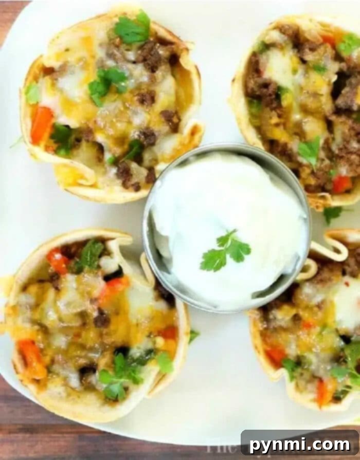 Steak fajita cups with ground beef, cheese, and veggies, served with a side of sour cream and garnished with fresh cilantro.