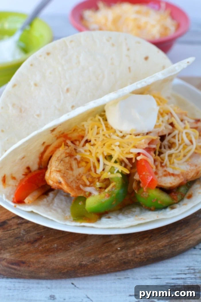 Easy Slow Cooker Chicken Fajitas 2 A colorful plate of crockpot chicken fajitas with sliced chicken, red and green bell peppers, and onions, garnished with fresh cilantro and lime wedges, ready to be served.