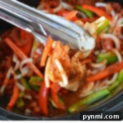 Tongs holding cooked chicken strips with bell peppers and onions in a skillet, showcasing the vibrant flavors of crockpot chicken fajitas.