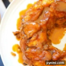 Close-up of a glazed pumpkin monkey bread ring on a white plate, with a caramel-like drizzle on top. Made using cinnamon rolls, it offers layers of spicy sweetness perfect for autumn indulgence.
