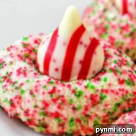 A close-up of a Hershey Kiss Christmas cookie, featuring a vibrant striped chocolate top and a festive coating of red and green sugar sprinkles, perfect for holiday celebrations.