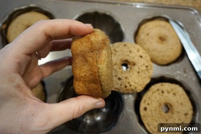 A hand gently holds a small pumpkin cake crafted from cake mix over a tray adorned with mini Bundt cakes.