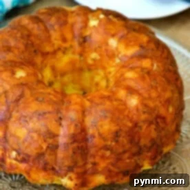 A golden brown breakfast bundt cake sits elegantly on a glass platter, with a knife poised nearby and a blue napkin adding a touch of color in the background.