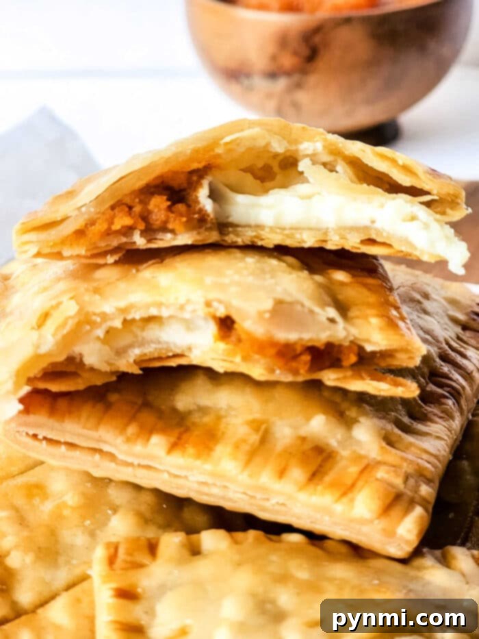 A beautifully arranged selection of pumpkin hand pies, some with glaze, on a white plate with fall decor.