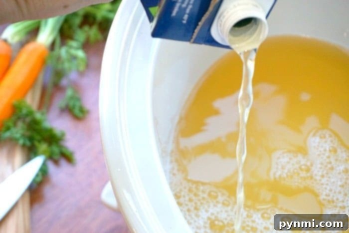 Chicken broth being poured into a slow cooker containing chopped carrots and other ingredients for an Italian wedding soup recipe.