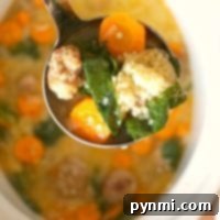 A ladle of easy Italian wedding soup with meatballs, carrots, spinach, and couscous hovers over a bowl.