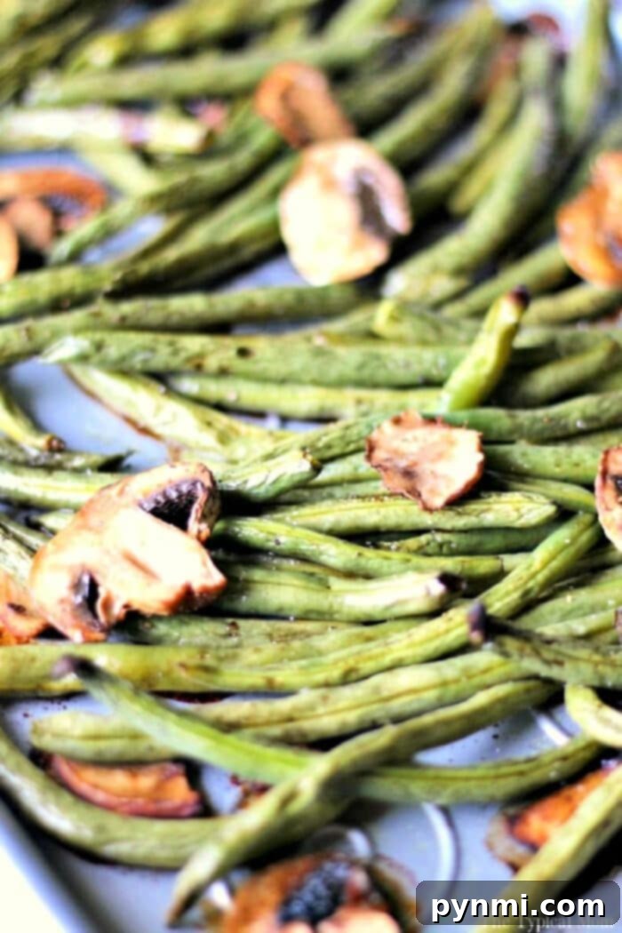 A vibrant medley of fresh green beans and sliced mushrooms roasted on a sheet pan, seasoned to perfection.