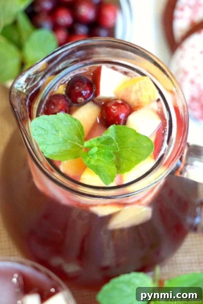Sparkling Cranberry Sangria: A festive and refreshing drink perfect as a mocktail or cocktail for all seasons. A beautiful pitcher of sparkling cranberry sangria, garnished with fresh cranberries, apple slices, and mint, ready to be served.