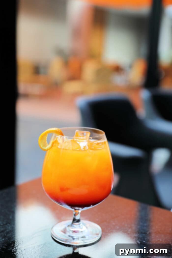 A vibrant sparkling island cocktail with a citrus twist sits on a reflective table in a stylish, blurred background setting.