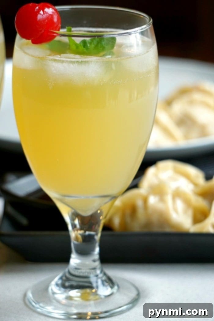 A glass of sparkling malibu by breeze, elegantly garnished with a cherry and mint, sits enticingly in the foreground, while savory dumplings temptingly linger in the background.