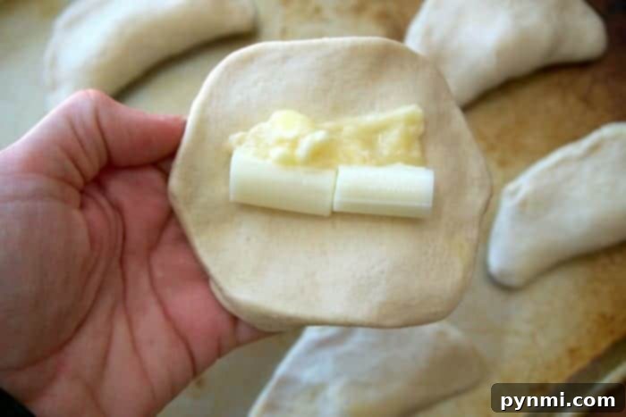 Gooey Cheese Filled Biscuit Bombs 4 A flattened refrigerated biscuit dough on a cutting board, with pieces of string cheese and a spoonful of garlic butter placed in the center, ready to be folded.