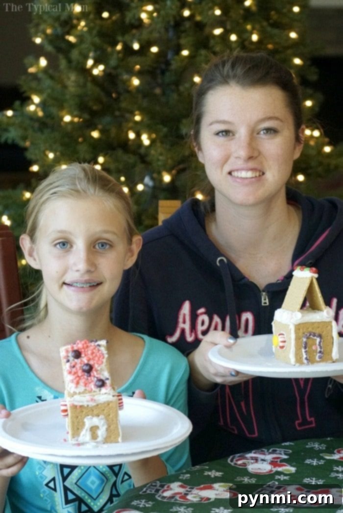 DIY Gingerbread House Kit complete with free printable so you can create some yourself this Christmas. Great activity for holiday parties. Two children proudly displaying their finished DIY gingerbread houses, full of colorful candies and joyful expressions.