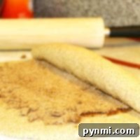 A delicious dough is being skillfully rolled with cinnamon and sugar, hinting at the creation of irresistible gingerbread cinnamon rolls, with a trusty rolling pin in the background.
