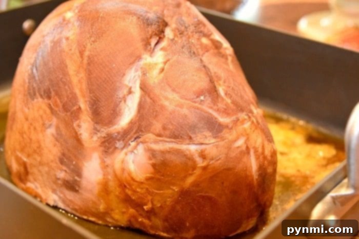 A pre-sliced, fully cooked ham resting in a deep roasting pan, ready for glazing and baking.