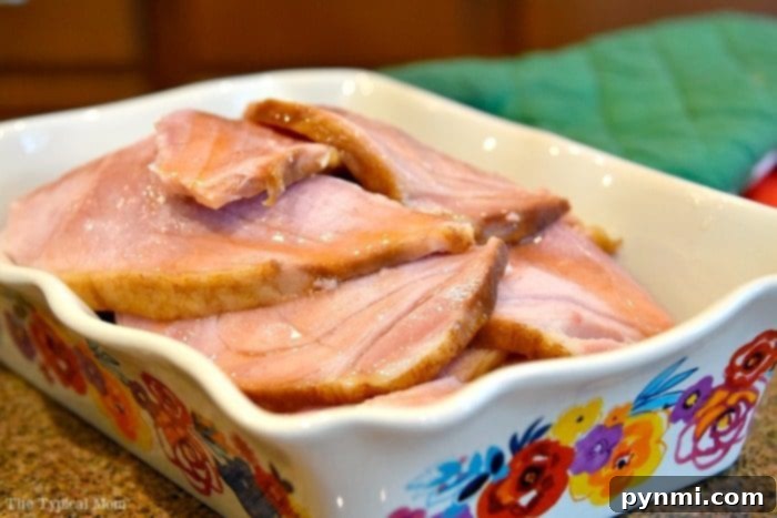 Sliced oven-baked ham served on a decorative white platter, showcasing its moist texture and rich glaze.