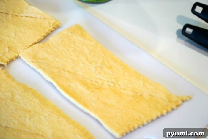 Ham and Cheese Crescent Roll-Ups 2 Unrolled crescent dough triangles on a cutting board, ready for filling.