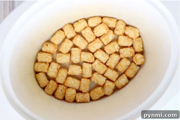 A slow cooker filled with the layered ingredients of a tater tot casserole, ready for cooking.