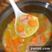 A ladle of slow cooker split pea soup with ham and carrots over a crockpot, illustrating the rich texture of the soup.
