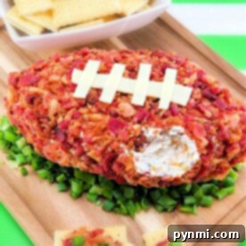 A football-shaped cheese ball, perfectly covered in crispy bacon, rests on a bed of fresh greens with white crackers elegantly arranged on a wooden board.