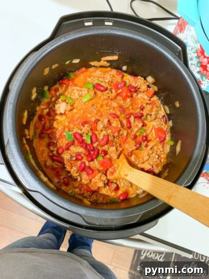 Easiest Instant Pot chili recipe ever and costs less than $10 total to make. Healthy pressure cooker dinner that even my kids go crazy over! We make this at least once a week and serve it as is topped with cheese or on top a bowl of rice. #instantpot #chili #easy #best #dump #instantpotrecipes #thetypicalmom #instantpotchili #crockpotexpress A large pot of rich, thick Instant Pot chili, ready to be served, topped with shredded cheese and fresh cilantro.