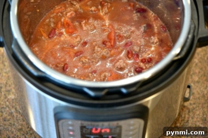 Easiest Instant Pot chili recipe ever and costs less than $10 total to make. Healthy pressure cooker dinner that even my kids go crazy over! We make this at least once a week and serve it as is topped with cheese or on top a bowl of rice. A simple white seasoning packet labeled 'Chili Seasoning' rests on a wooden surface next to a bowl of chili, highlighting the convenience of the 5-ingredient recipe.