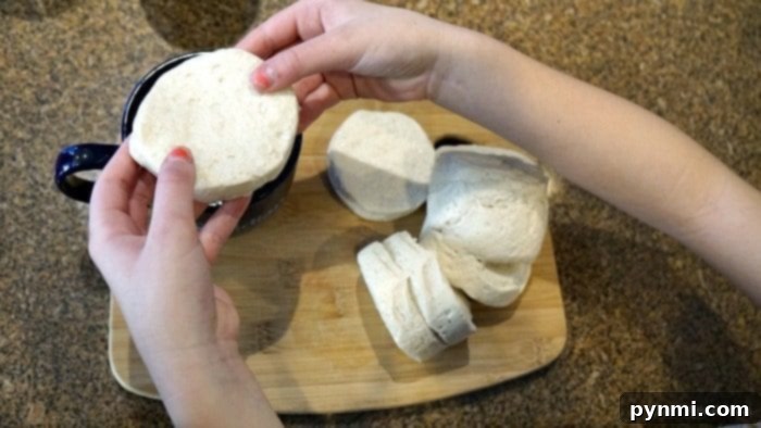 Hands holding biscuit dough over a cutting board with more dough pieces, illustrating the simplicity of preparing the crust for the quick pizza in a mug recipe.