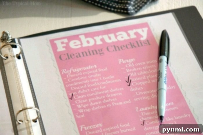 A home organization binder lies open to a page titled February Cleaning Checklist, a black pen resting on top. Tasks under categories like Refrigerator and Freezer are itemized with checkmarks, showcasing a well-structured plan for household cleanliness and efficiency.