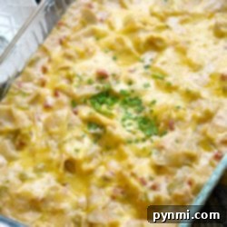 A cheesy chicken tortilla bake topped with chopped green herbs in a glass baking dish.