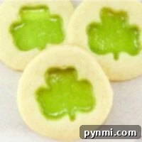 Learn how to make stained glass cookies with three delightful treats featuring green shamrock-shaped translucent centers, elegantly displayed on a light surface.