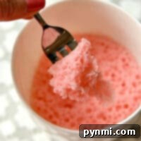 A fork holding a piece of fluffy strawberry cake from a white mug.