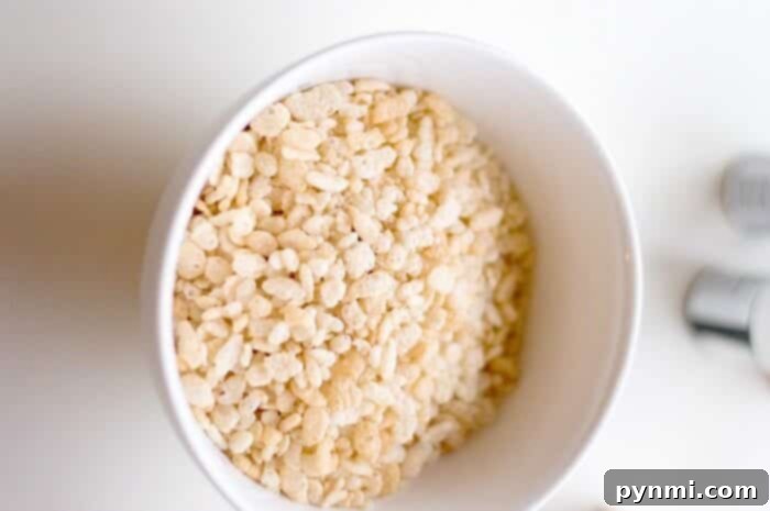 A white bowl filled with puffed rice cereal is placed on a white surface, showcasing the primary ingredient for Rice Krispy Treats.