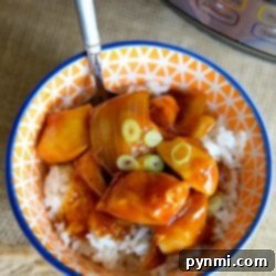 A bowl of rice topped with saucy orange chicken and green onions, showcasing instant pot orange chicken recipe perfection, sits invitingly next to a pressure cooker.
