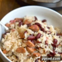 A bowl of rice with kidney beans and sausage, served with a spoon. The Instant Pot red beans and rice dish adds a delightful touch, prominently featured in the background.