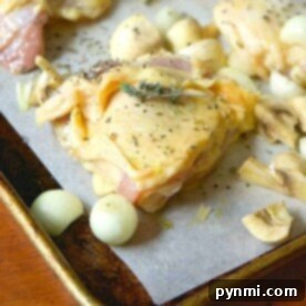 Oven-baked chicken thighs, mushrooms, and onions rest on a parchment-lined baking sheet, sprinkled with fragrant herbs.