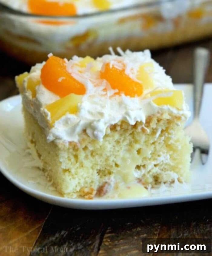 Close-up of a coconut pineapple poke cake slice, showing the moist layers, rich whipped topping, and tropical fruit garnishes.