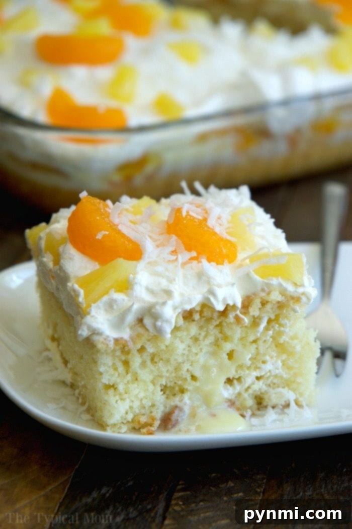 A beautifully presented slice of tropical poke cake on a white plate, showcasing its moist interior, vibrant fruit topping, and shredded coconut.