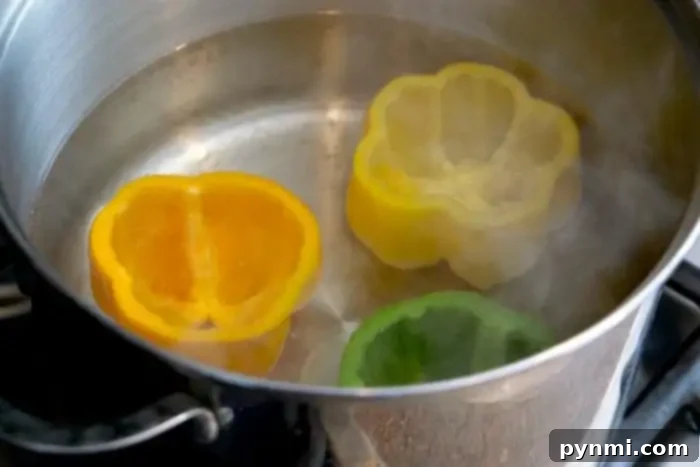 Slices of yellow, orange, and green bell peppers are boiling in a pot of water on the stove, demonstrating how to blanch bell peppers perfectly. Steam rises from the pot.