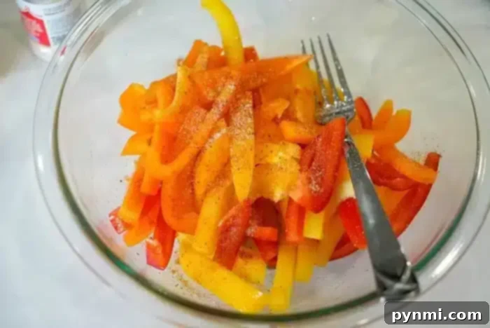 A glass bowl brimming with vibrant, sliced red, yellow, and orange bell peppers is artfully seasoned. If you're curious about prepping them further, learning how to blanch bell peppers can enhance their texture. A fork and spoon are nestled inside the bowl for easy serving.