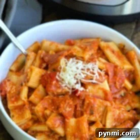 A bowl of rigatoni pasta with a tangy tomato sauce and a generous sprinkle of grated cheese sits invitingly in front of an Instant Pot, bringing to mind the delightful flavors of pizza in every bite.