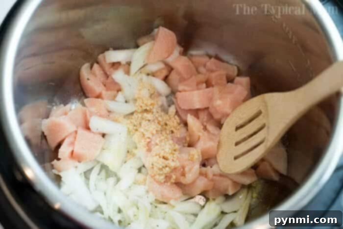 Chopped chicken, onions, and minced garlic simmer in a pot with a wooden spoon—the perfect start for an instant pot white chicken chili.