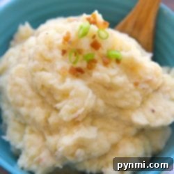 A bowl of creamy pressure cooker mashed potatoes, garnished with fresh chopped green onions and crispy bacon bits, with a wooden spoon ready for serving.