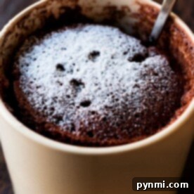 Chocolate mug cake recipe with powdered sugar and a spoon, served in a beige mug on a wooden surface.